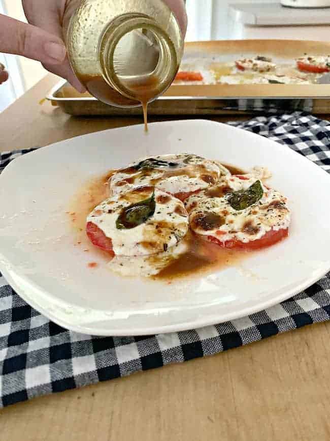 pouring balsamic dressing over baked tomatoes and mozzarella on plate