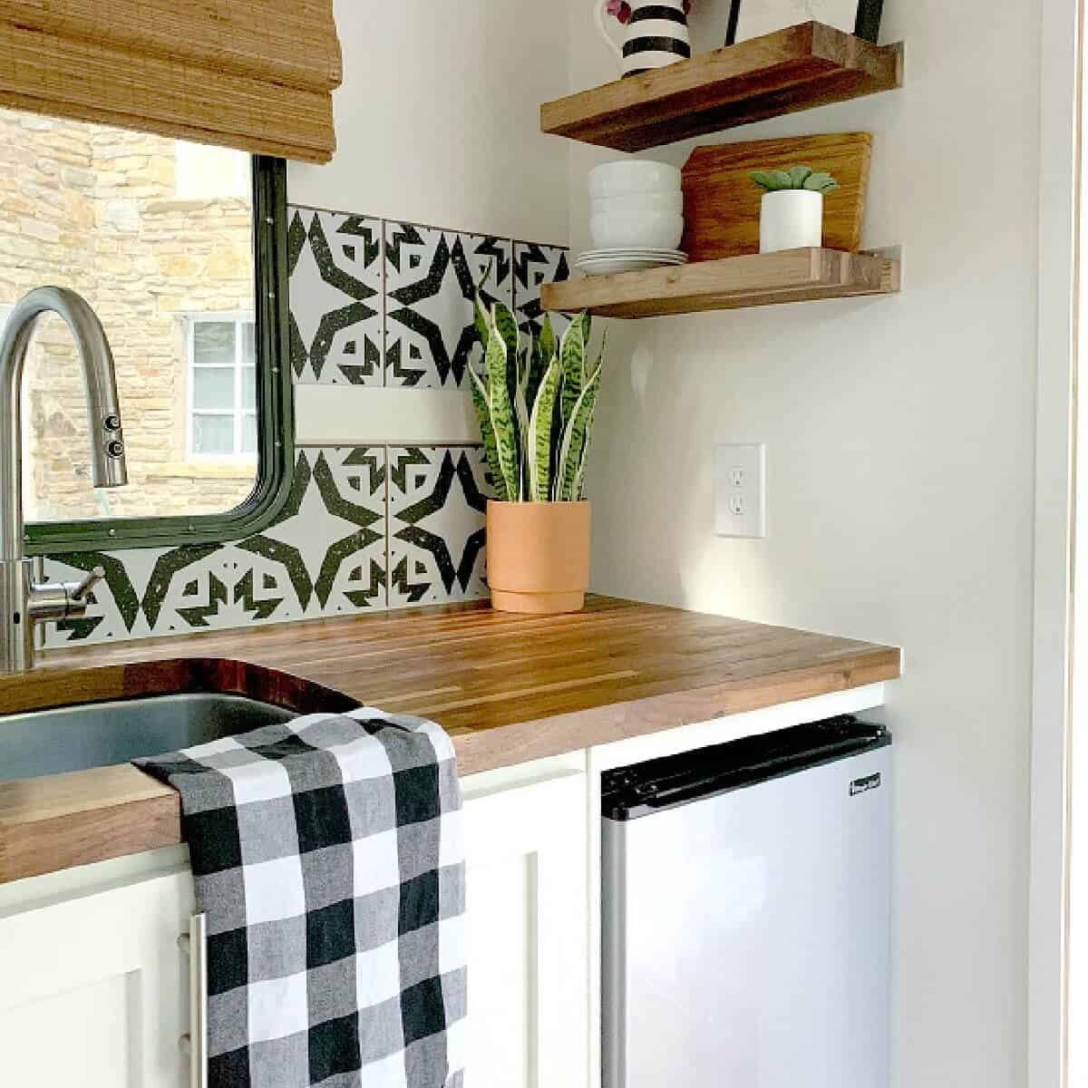 tiny RV kitchen with removable wallpaper backsplash, plant in corner and black and white towel on sink