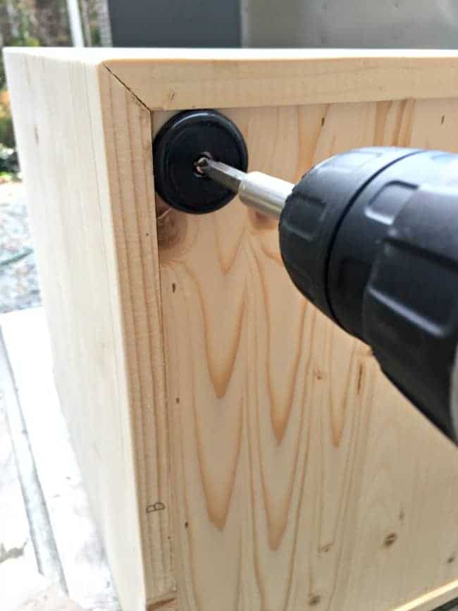 using a drill to install rubber feet on bottom of storage ottoman