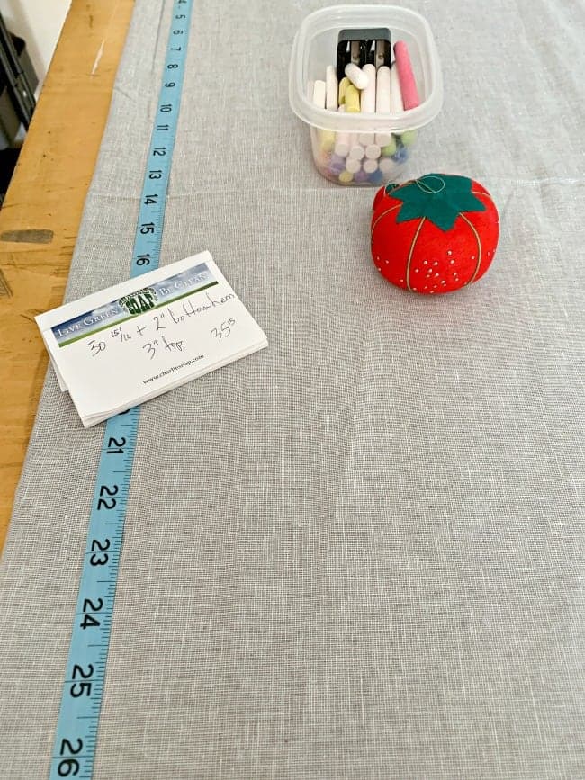 gray fabric for no sew curtain with tape measure, straight pins and bowl of chalk