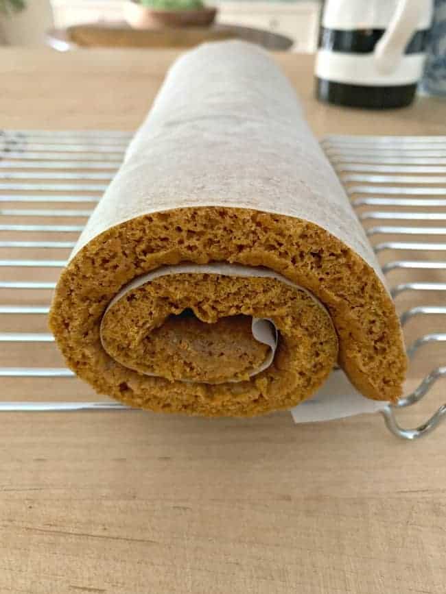 pumpkin cake rolled up in parchment paper cooling on baking rack