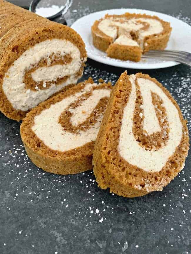 easy pumpkin roll with mascarpone cream filling sliced and sitting on a black counter with powdered sugar sprinkled on it