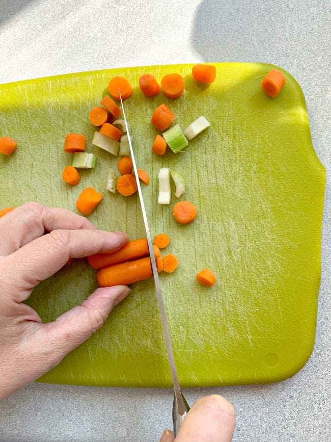 chopping carrots and celery on a green cutting board