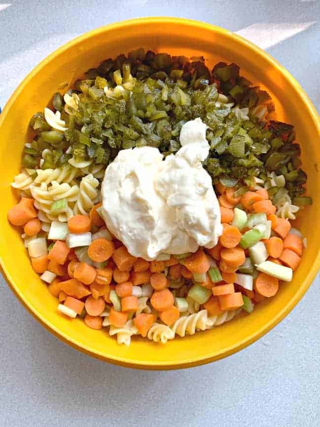 overhead view of tuna pasta salad recipe with chopped carrots and celery, sweet pickles and a big dollop of mayonnaise