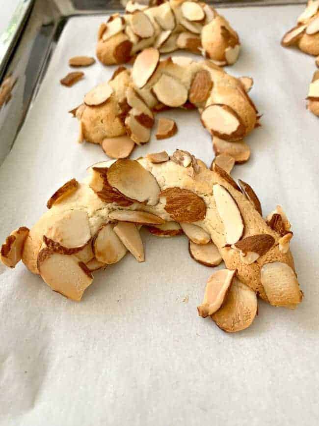 freshly baked almond horn cookies cooling on a parchment paper cookie sheet