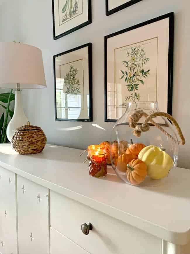 white cabinet with fall leaf candle holders, pumpkins and white lamp