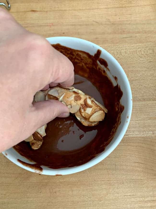 dipping almond horn cookies in a bowl of melted semi-sweet chocolate