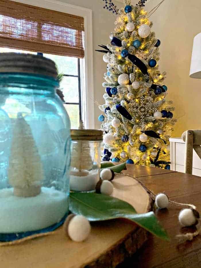 blue jar with bottle brush tree with flocked Christmas tree in background