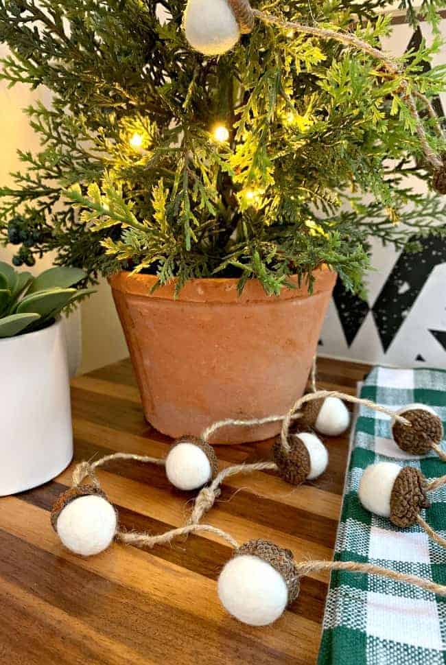 white felted acorn garland laying at the base of a potted faux tree