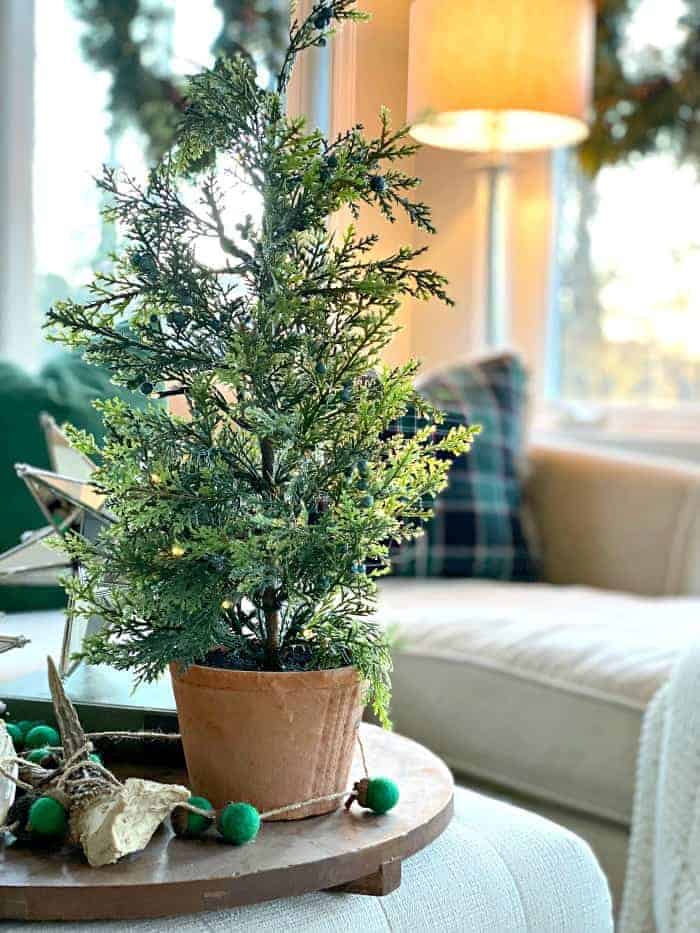 mini faux Christmas tree on ottoman in sunroom