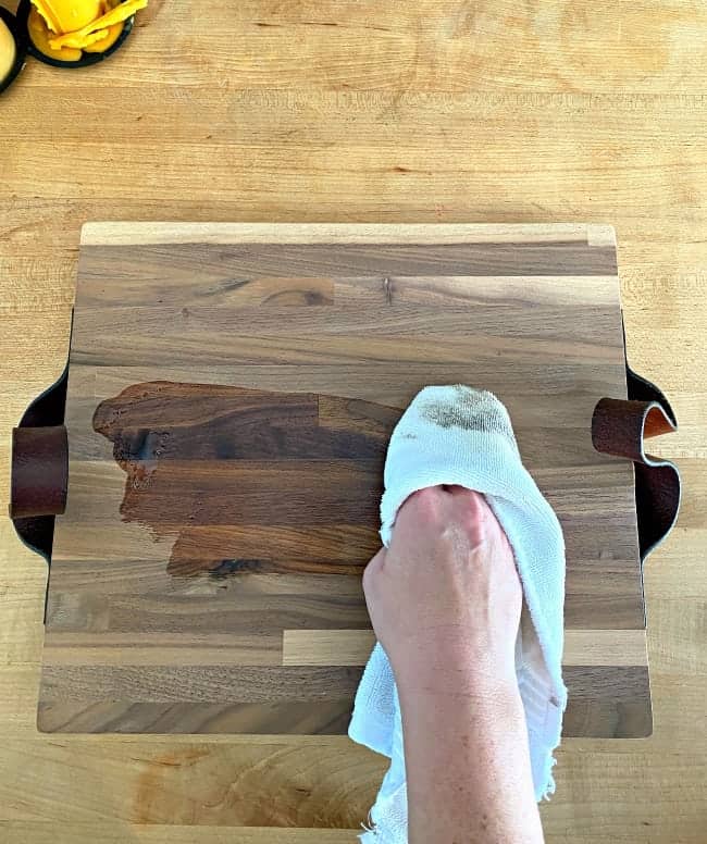 wiping wood conditioner on butcher block cutting board with white cloth