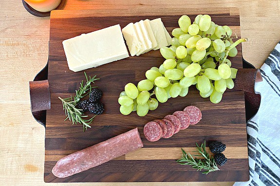 sliced meat and cheese, a bunch of grapes and blackberries on top of DIY butcher block cutting board