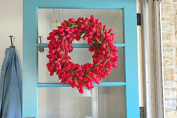 faux red tulip wreath hanging on turquoise painted front door