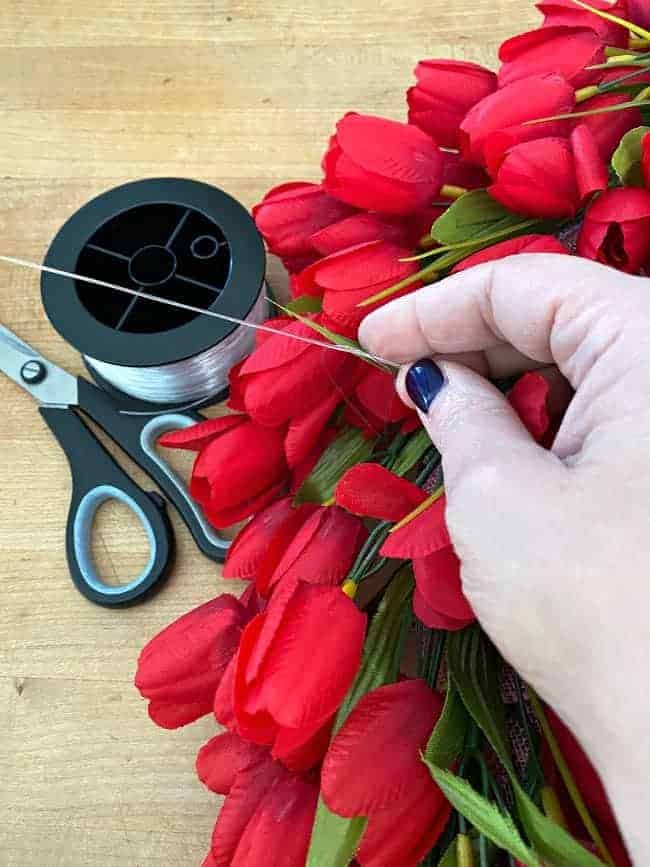 tying fishing line on faux red tulip wreath