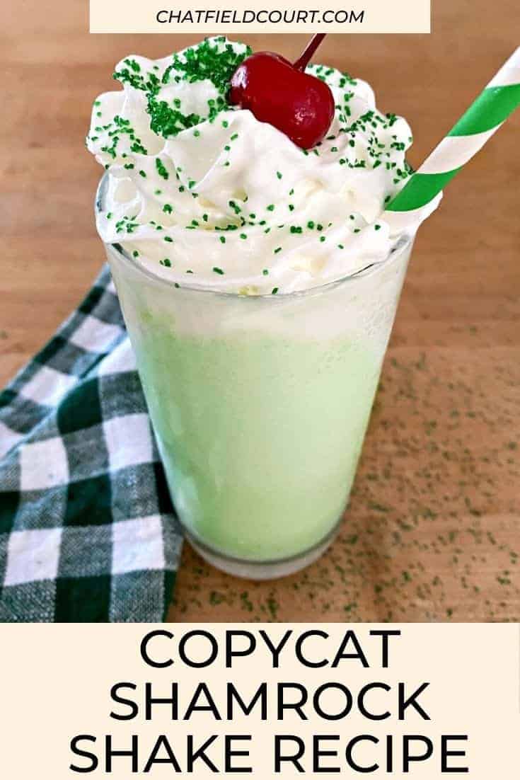 shamrock shake with whipped cream, cherry and green straw on butcher block countertop and large graphic