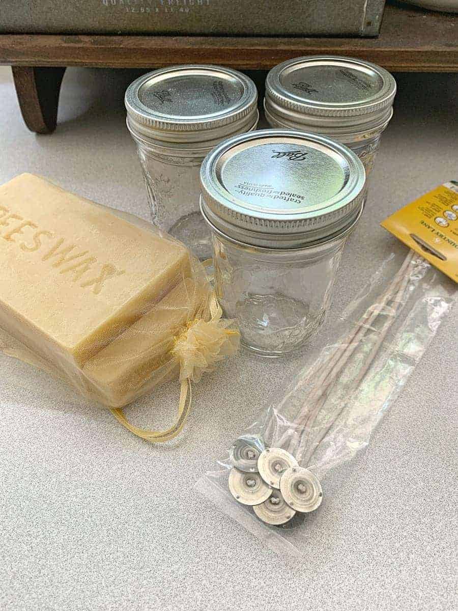 3 empty mason jars, a block of raw beeswax and cotton wicks on countertop