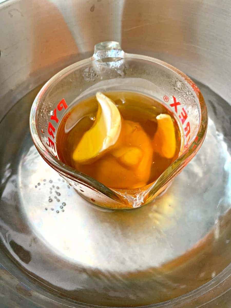 melted beeswax in glass measuring cup sitting in pot of hot water