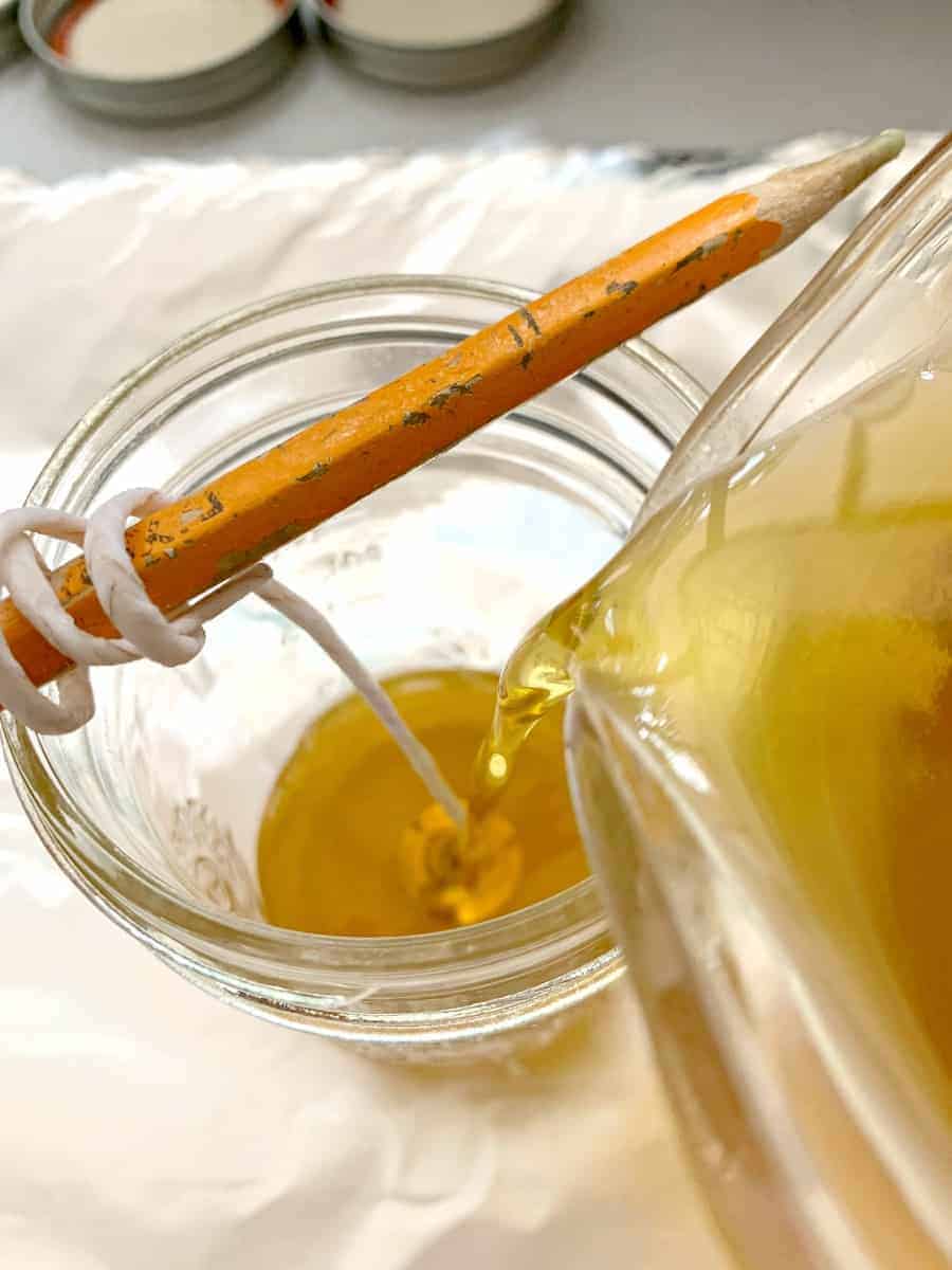 pouring melted beeswax into mason jar with cotton wick wrapped around pencil 