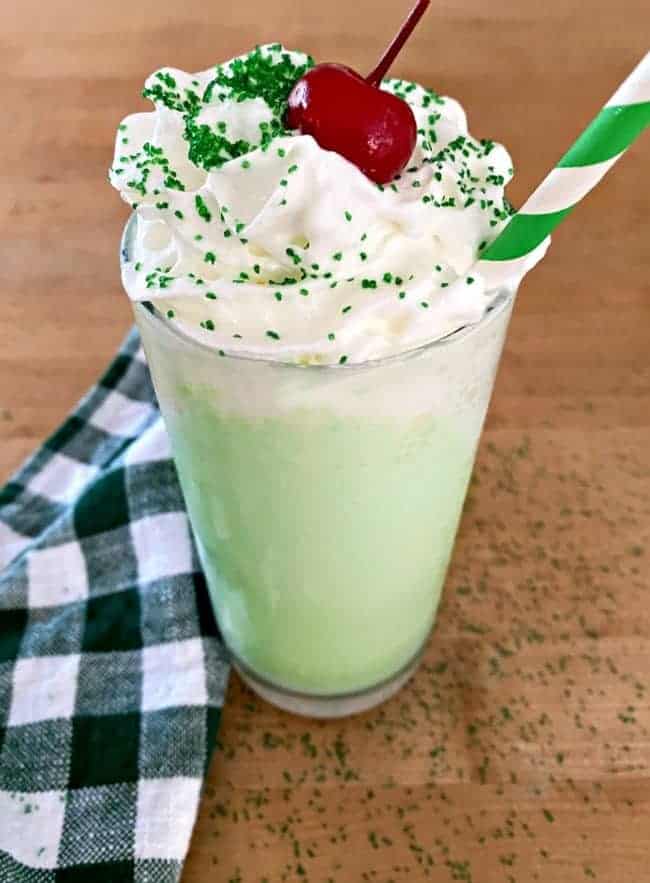 shamrock shake with whipped cream, cherry and green straw on butcher block countertop