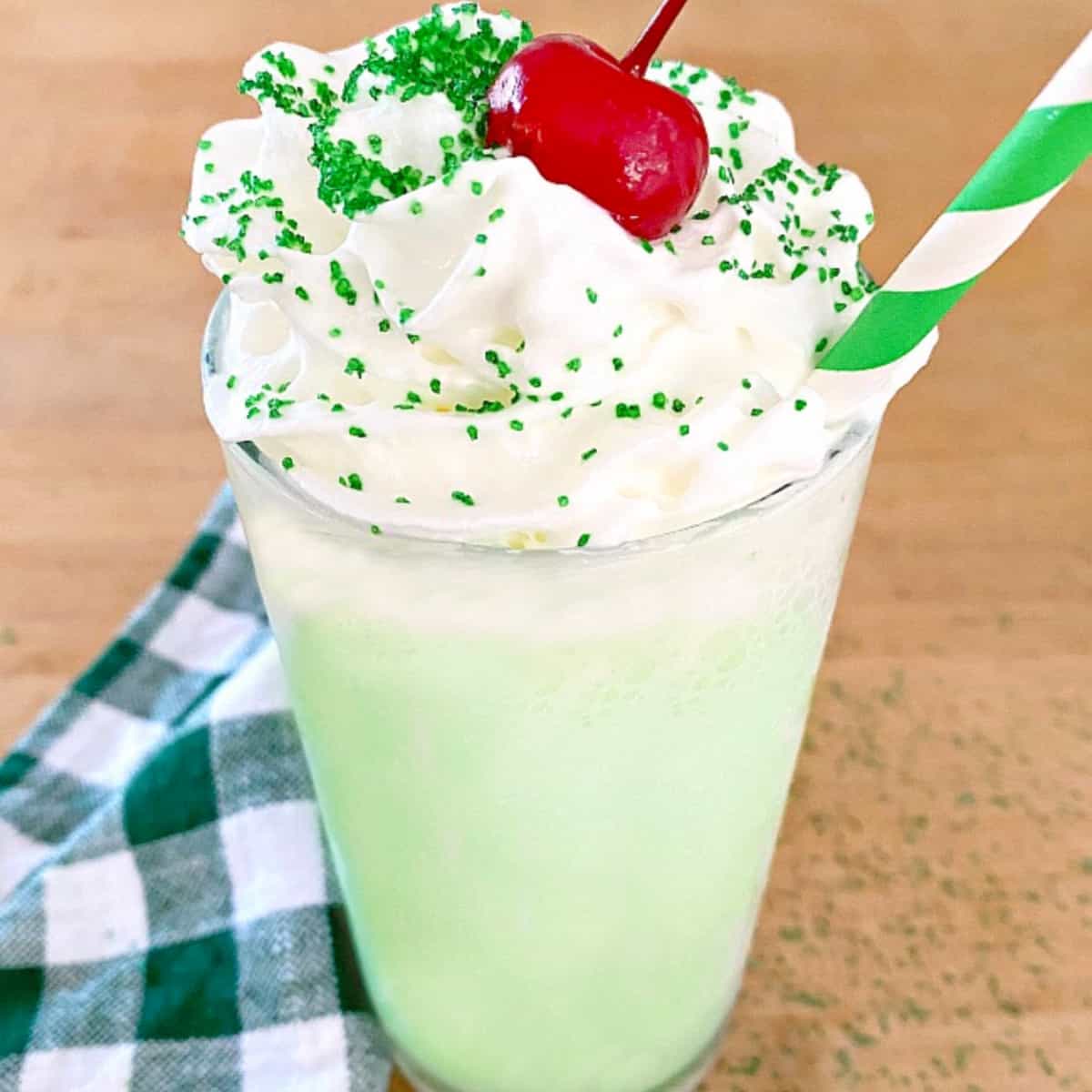 shamrock shake with whipped cream, cherry and green straw on butcher block countertop