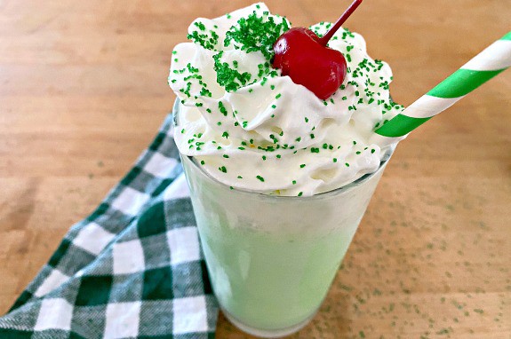 shamrock shake with whipped cream, cherry and green straw on butcher block countertop