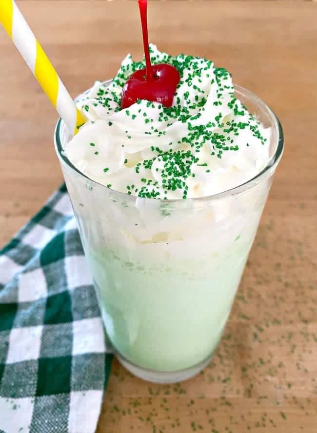 shamrock shake with whipped cream, cherry and green straw on butcher block countertop