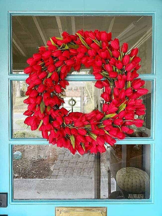 faux red tulip wreath hanging on turquoise painted front door