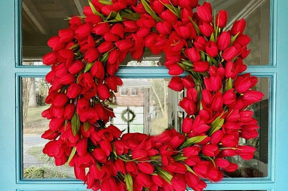 faux red tulip wreath hanging on turquoise painted front door