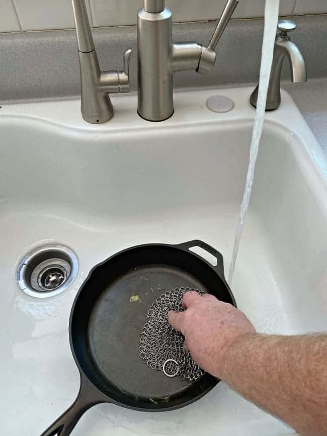 How to Clean a Cast Iron Pan pix cleaning a dirty cast iron pan in a sink with running water