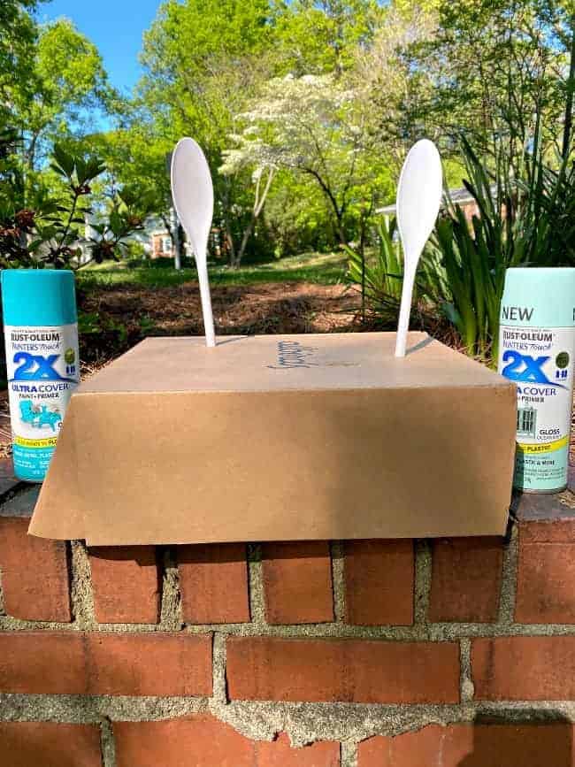 2 white plastic spoons stuck in a box top wiith a spray paint can on either side