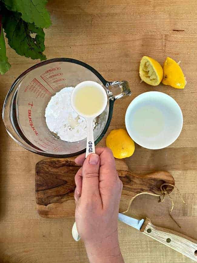 adding lemon juice to powdered sugar in a glass measuring cup