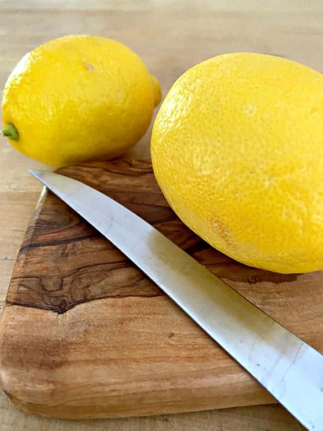 2 lemons with knife on cutting board