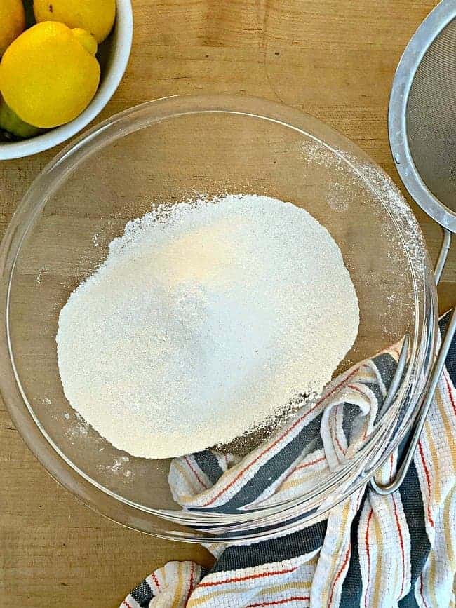 sifted flower in glass bowl with dish towel next to it, for lemon loaf recipe