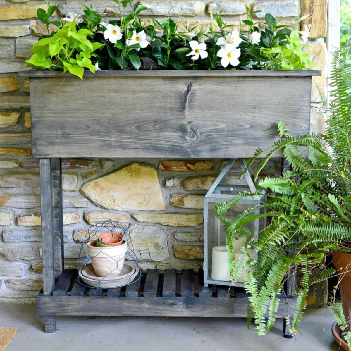 finished DIY wood raised planter box with legs with flowers planted in it and old pots on bottom shelf