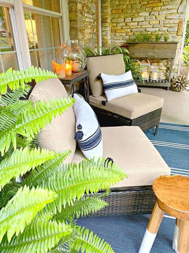 front porch of stone cottage with 2 wicker chairs with pillows on them and a striped blue rug on the ground