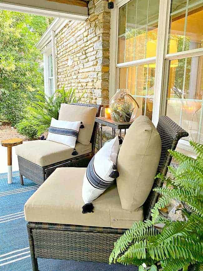 front porch of stone cottage with 2 wicker chairs with pillows on them and a striped blue rug on the ground