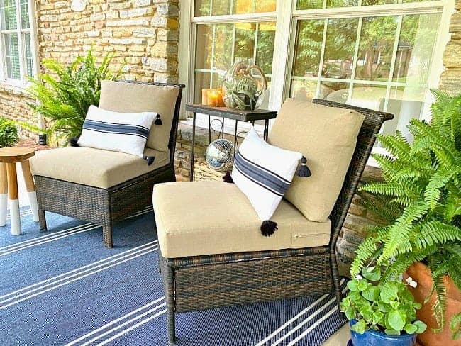 front porch of stone cottage with 2 wicker chairs with pillows on them and a striped blue rug on the ground