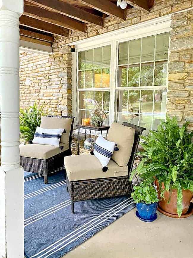 covered front porch decorated for summer with pillows on 2 chairs and a blue striped area rug