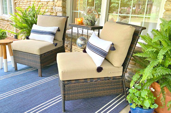 front porch of stone cottage with 2 wicker chairs with pillows on them and a striped blue rug on the ground