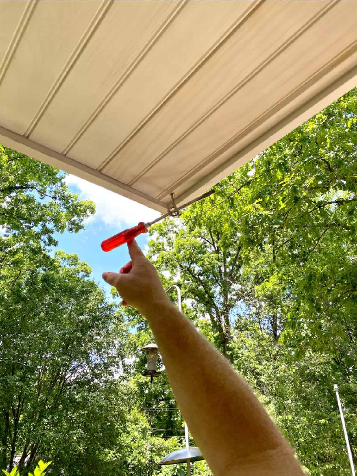 screwing an eye hook into a wood porch ceiling with a screwdriver