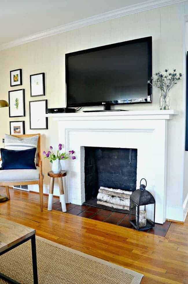 white painted fireplace with birch logs inside and a large tv on the mantle