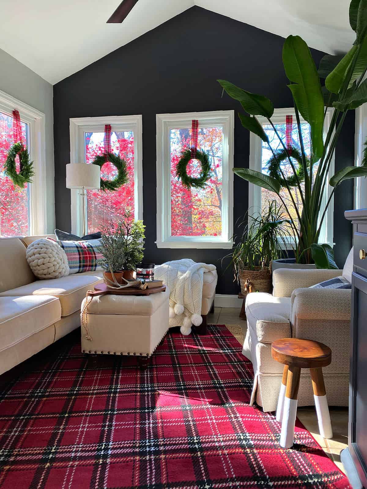 small sunroom decorated for Christmas with a red plaid rug and window wreaths