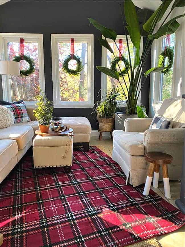 small sunroom decorated for Christmas with a red plaid rug and window wreaths