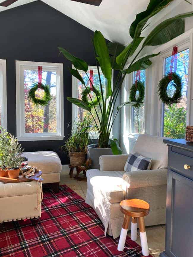 small sunroom decorated for Christmas with a red plaid rug and window wreaths