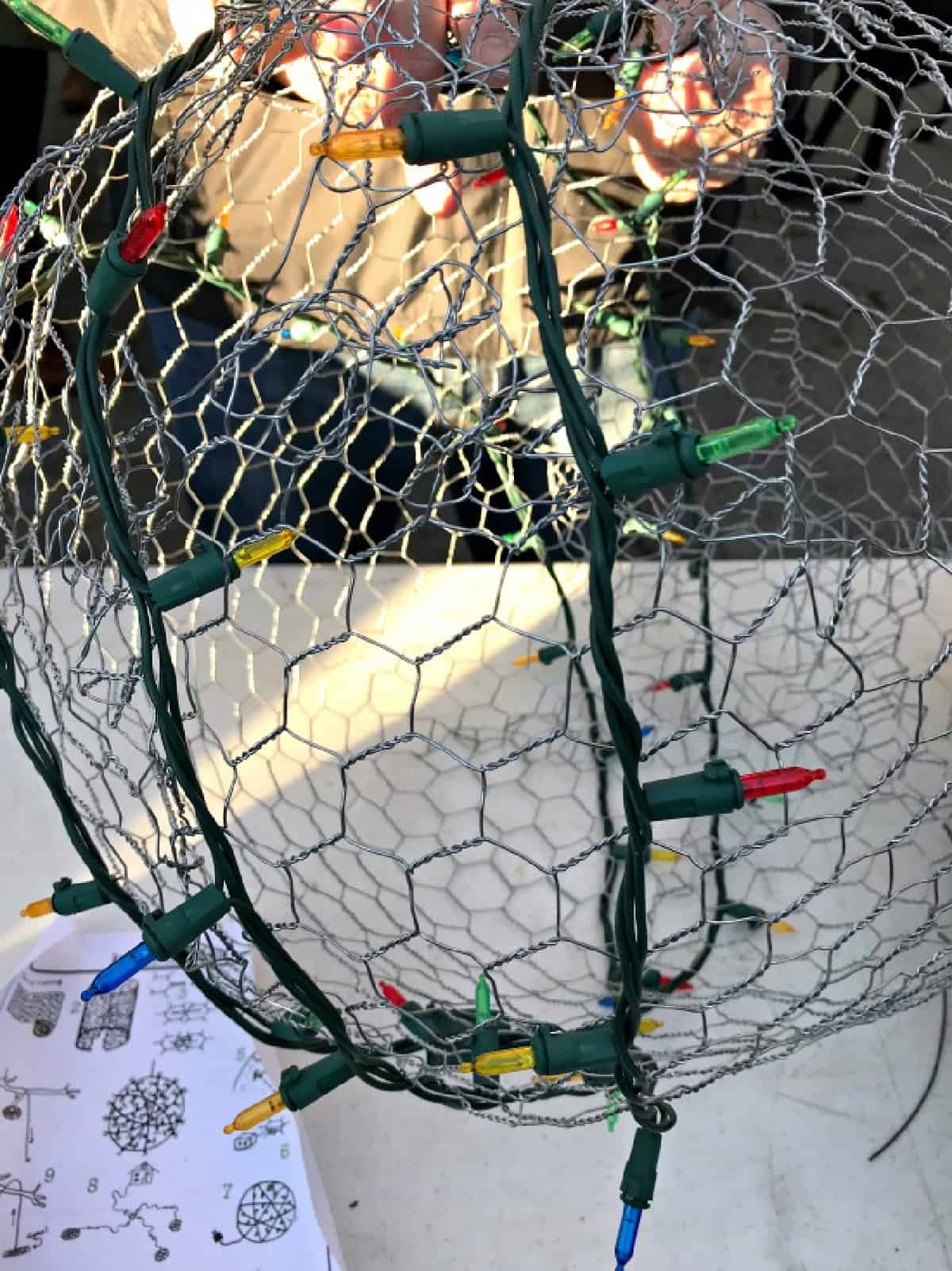 How to Make Lighted Christmas Balls (And How to Hang Them) shot wrapping Christmas lights on chicken wire ball form