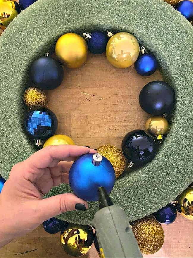 using hot glue gun to glue ornaments onto wreath