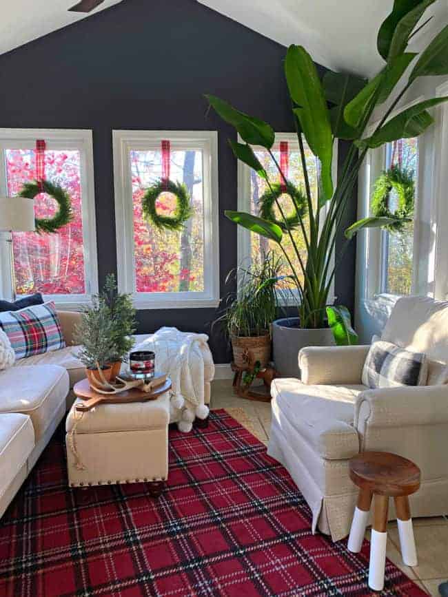 small sunroom decorated for Christmas with a red plaid rug and window wreaths