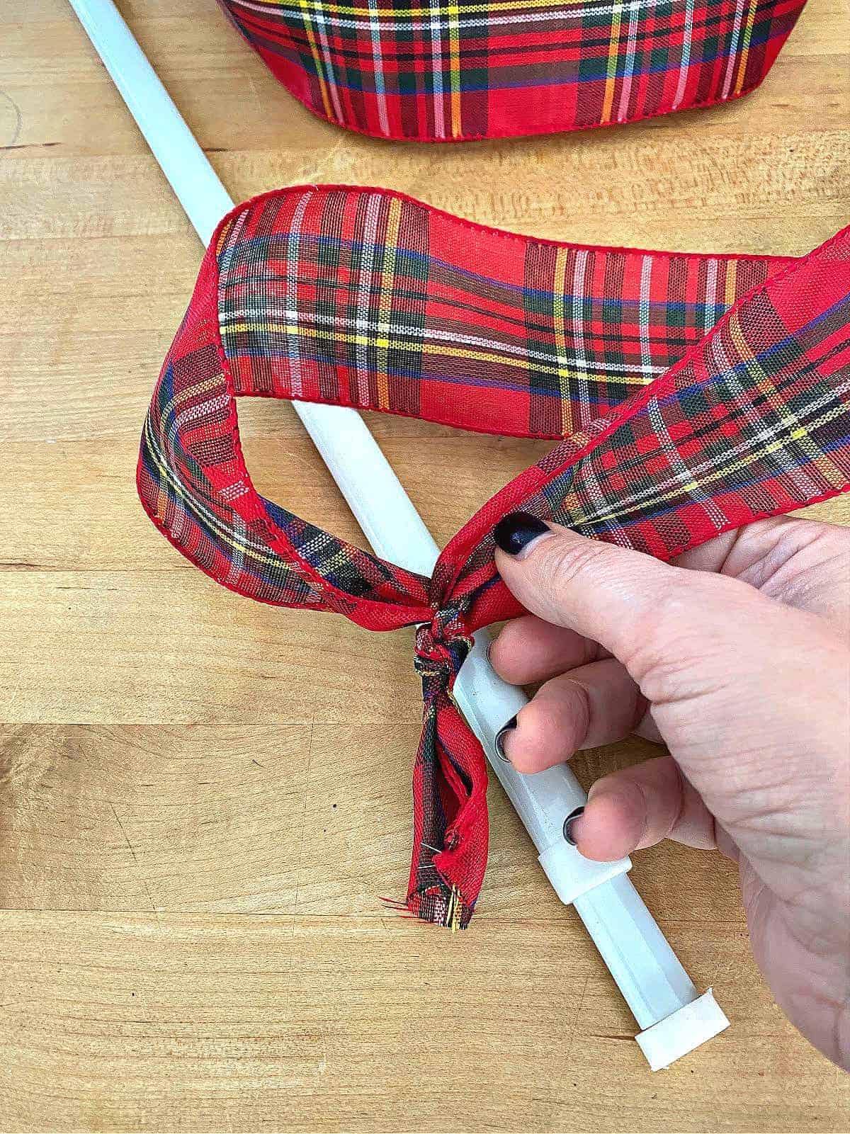 tying red checked ribbon to hang a wreath