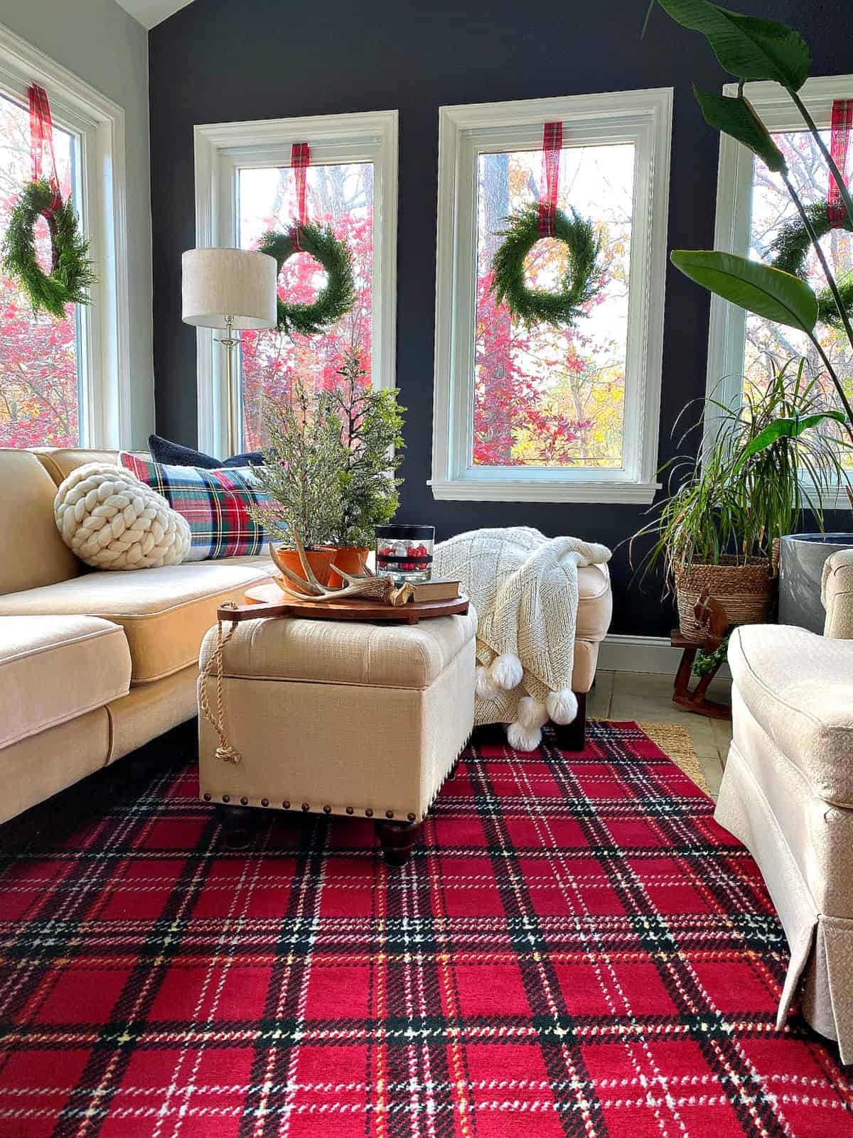 small sunroom decorated for Christmas with a red plaid rug and window wreaths