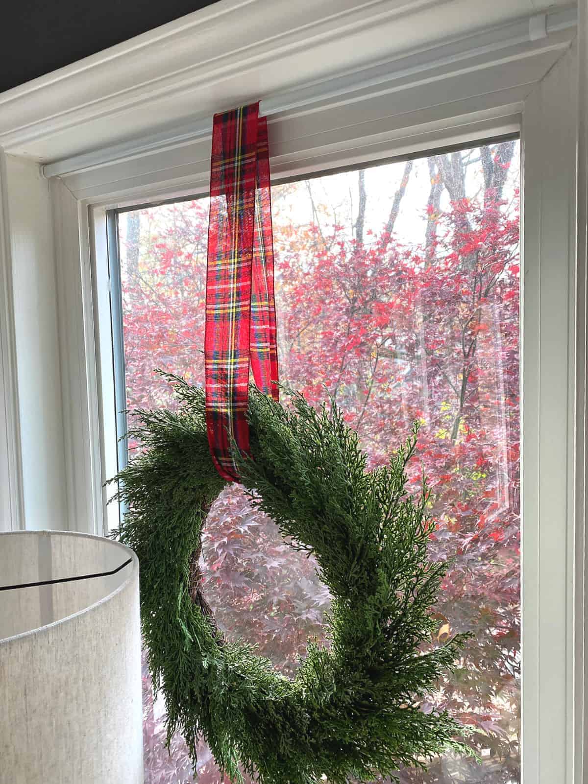 wreath hanging in window with red checked ribbon